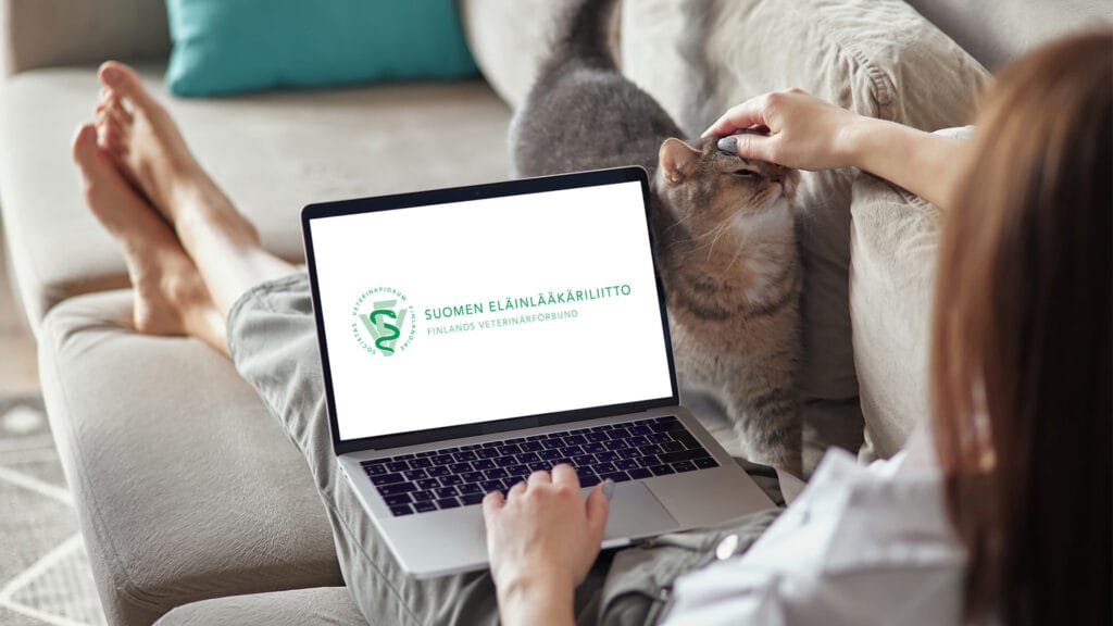 Nainen työskentelee kannettavalla tietokoneella ja silittää samalla sylissään olevaa kissaa.